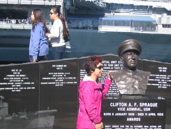 Tourist poses near bust of Vice Admiral Clifton Sprague.