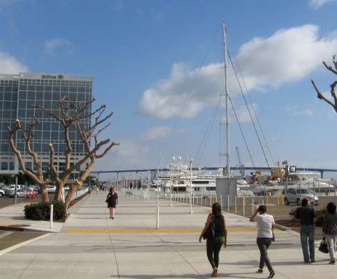 People walk toward Hilton hotel and giant mast of a world-record super yacht.