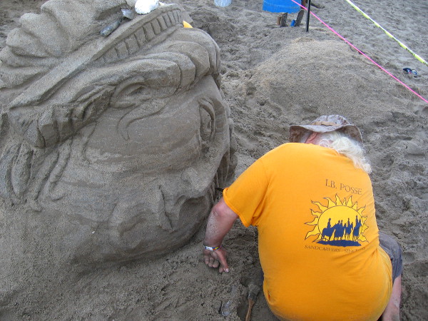 Sand sculptor is closely watched by the unblinking eyes of an inanimate subject.