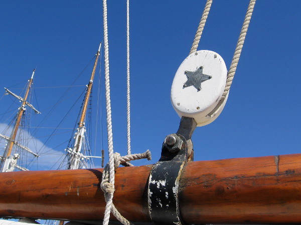 Star motif on a block used by a single rope in the complicated rigging. Masts of another nearby tall ship rise in the background.