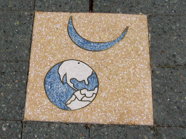 The Earth and a crescent moon. One of 26 terrazzo inserts arranged in a circle in the entrance plaza of the Balboa Park Activity Center. Created in 1999 by artist Joyce Cutler-Shaw.