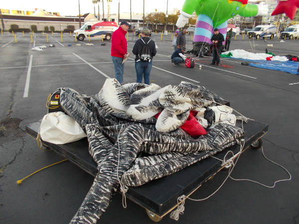 A balloon has been wheeled on a platform across the parking lot, waiting its turn to be inflated.