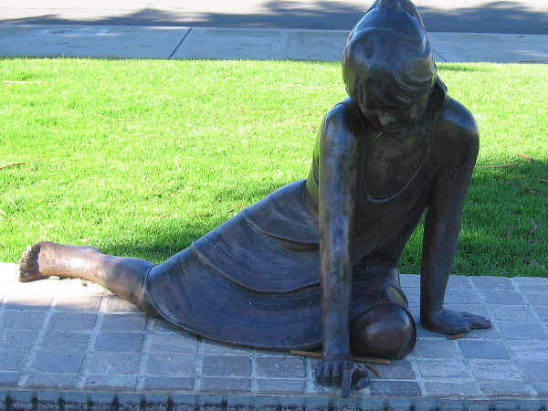 Bronze sculpture of young girl dipping finger into shallow basin of water. The Ellen Browning Scripps Memorial is located at the La Jolla Recreation Center.