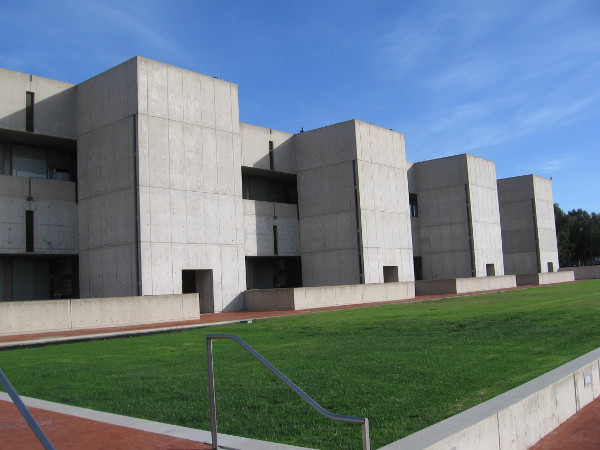 A monumental building made of smooth exposed concrete with simple, clean lines, between green grass and blue San Diego sky.
