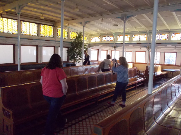 Visitors aboard the Berkeley look at the beautiful long wooden benches and stained glass windows of the upper passenger deck.