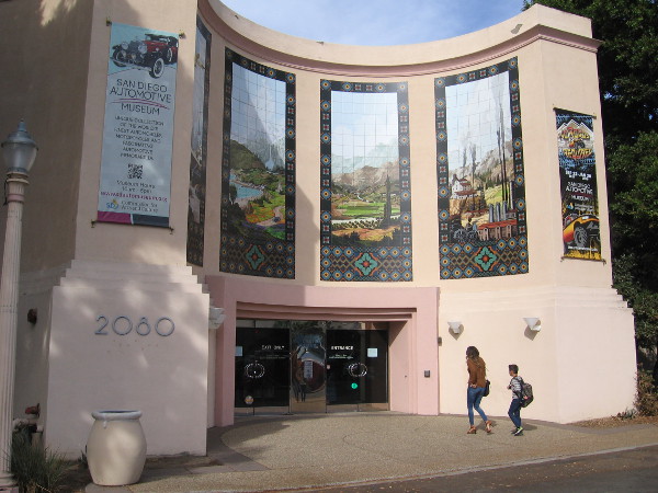 Visitors to the San Diego Automotive Museum in Balboa Park walk under four large temporary murals recently installed above the California State Building's entrance.