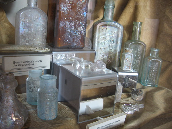 Excavated objects include jars, bottles, glass stoppers and a bone toothbrush handle. Names of medical remedies include Hamlin's Wizard Oil and Dr. J.H. McLean's Volcanic Oil.