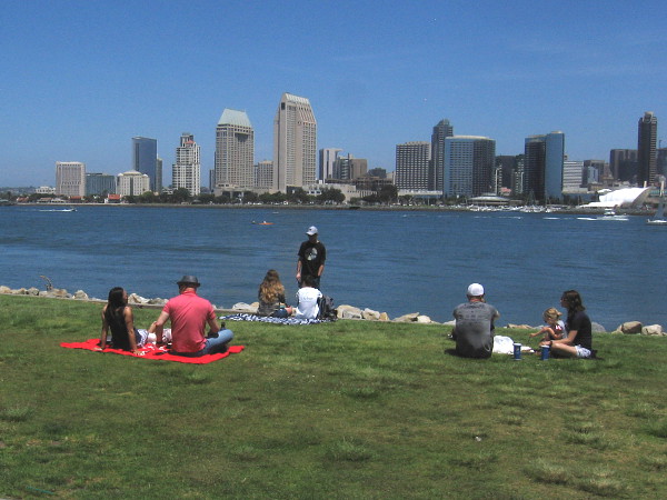 People sit on the grass at the Coronado Ferry Landing looking across San Diego Bay during the coronavirus pandemic.